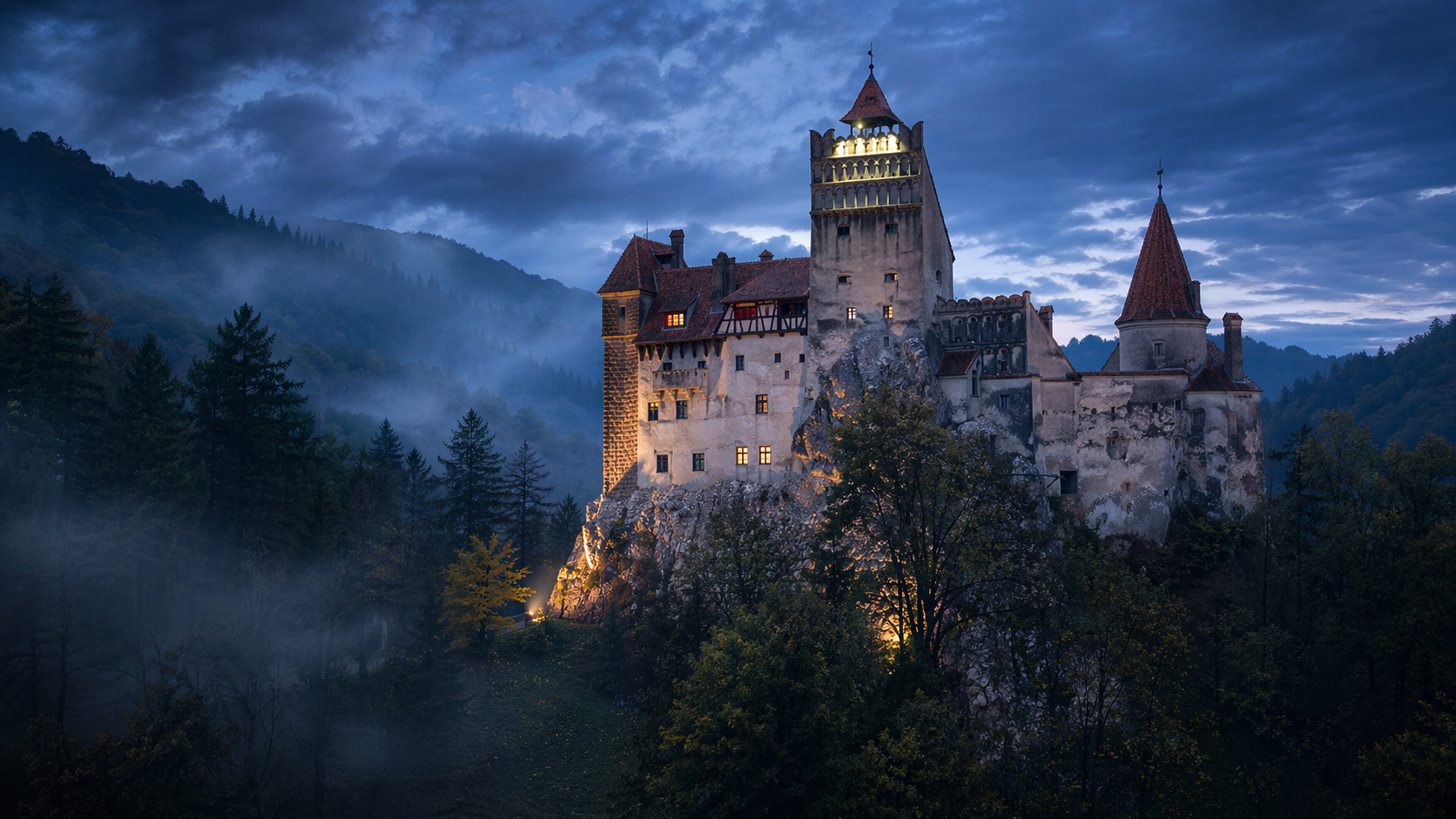 Bran Castle above dark forest at blue hour with mist behind.