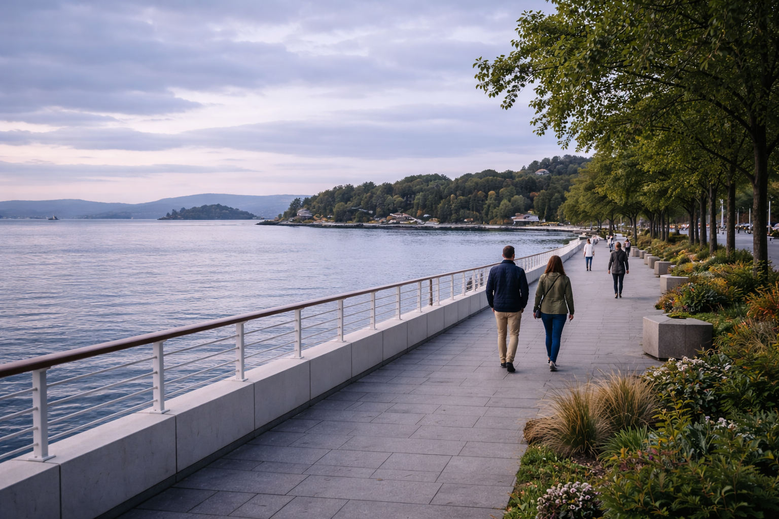 Oslo waterfront promenade beside the fjord with calm water and green shoreline beyond.