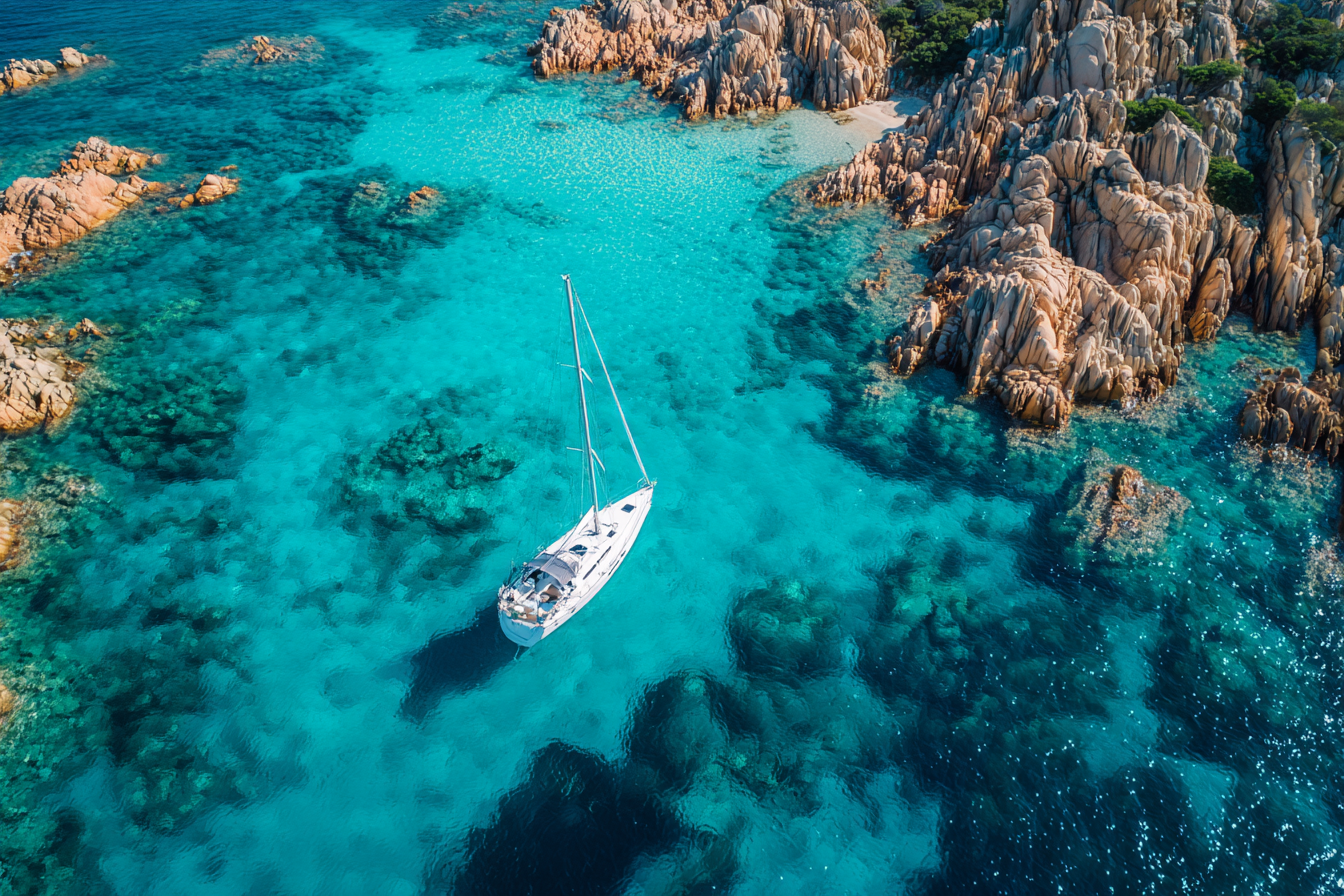 A sailboat in the clear turquoise waters of Sardinia, highlighting sailing and water sports in Italy.