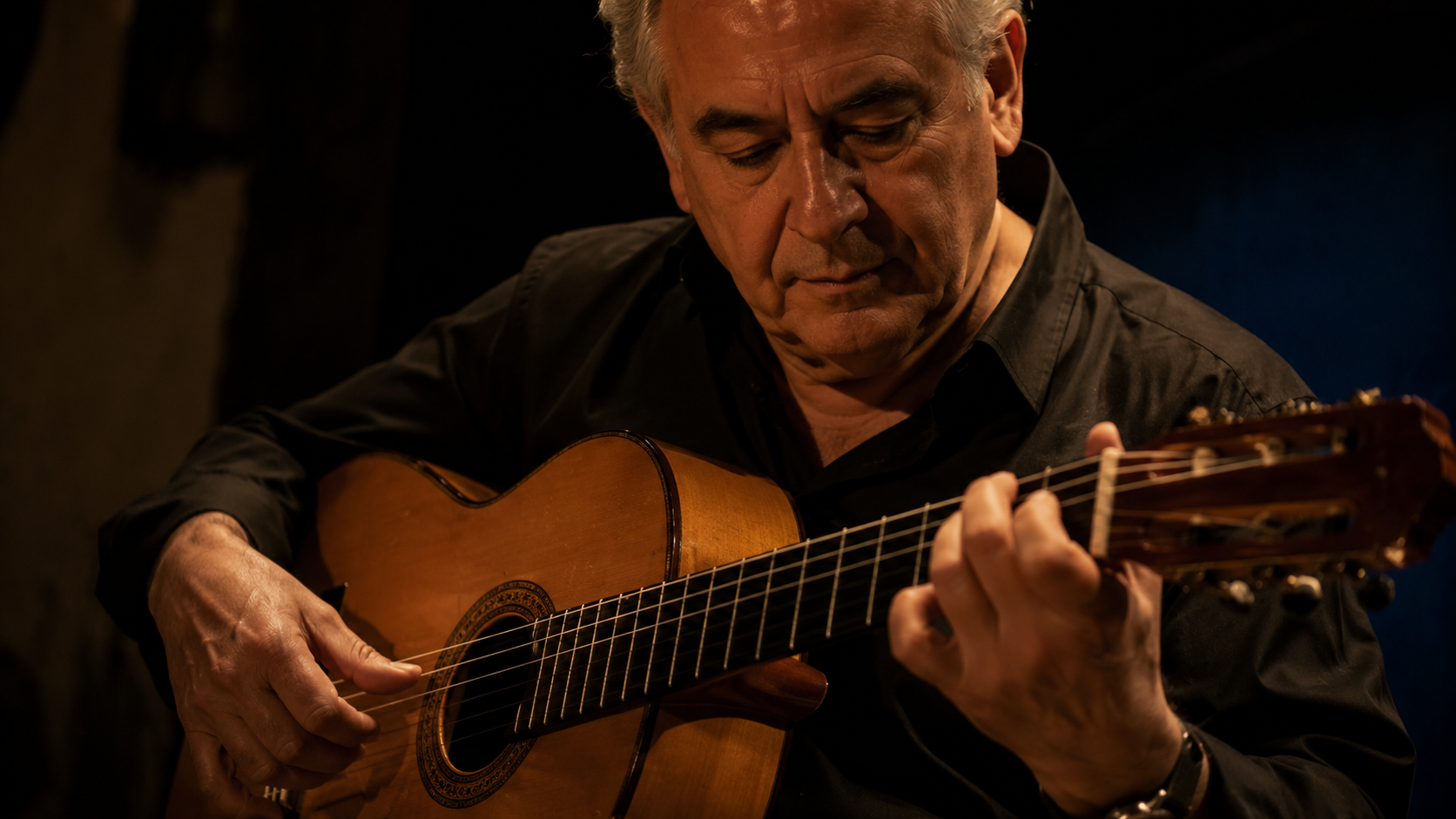 Older flamenco guitarist playing toque with focused precision.