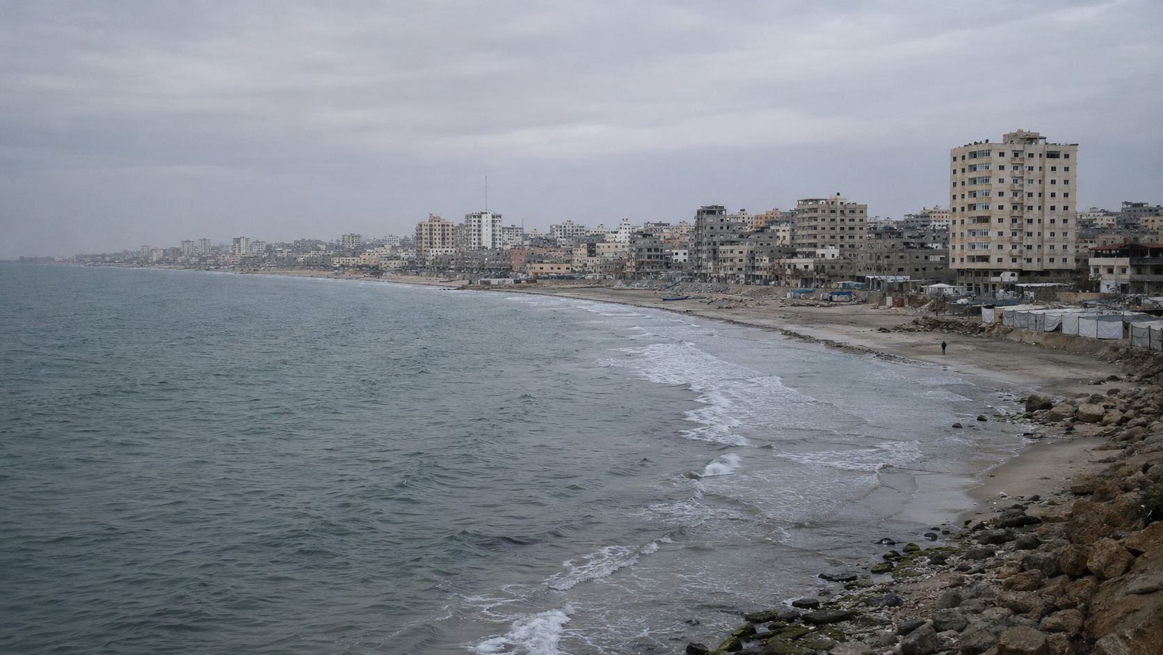Gaza coastline under overcast light with dense city buildings in the distance