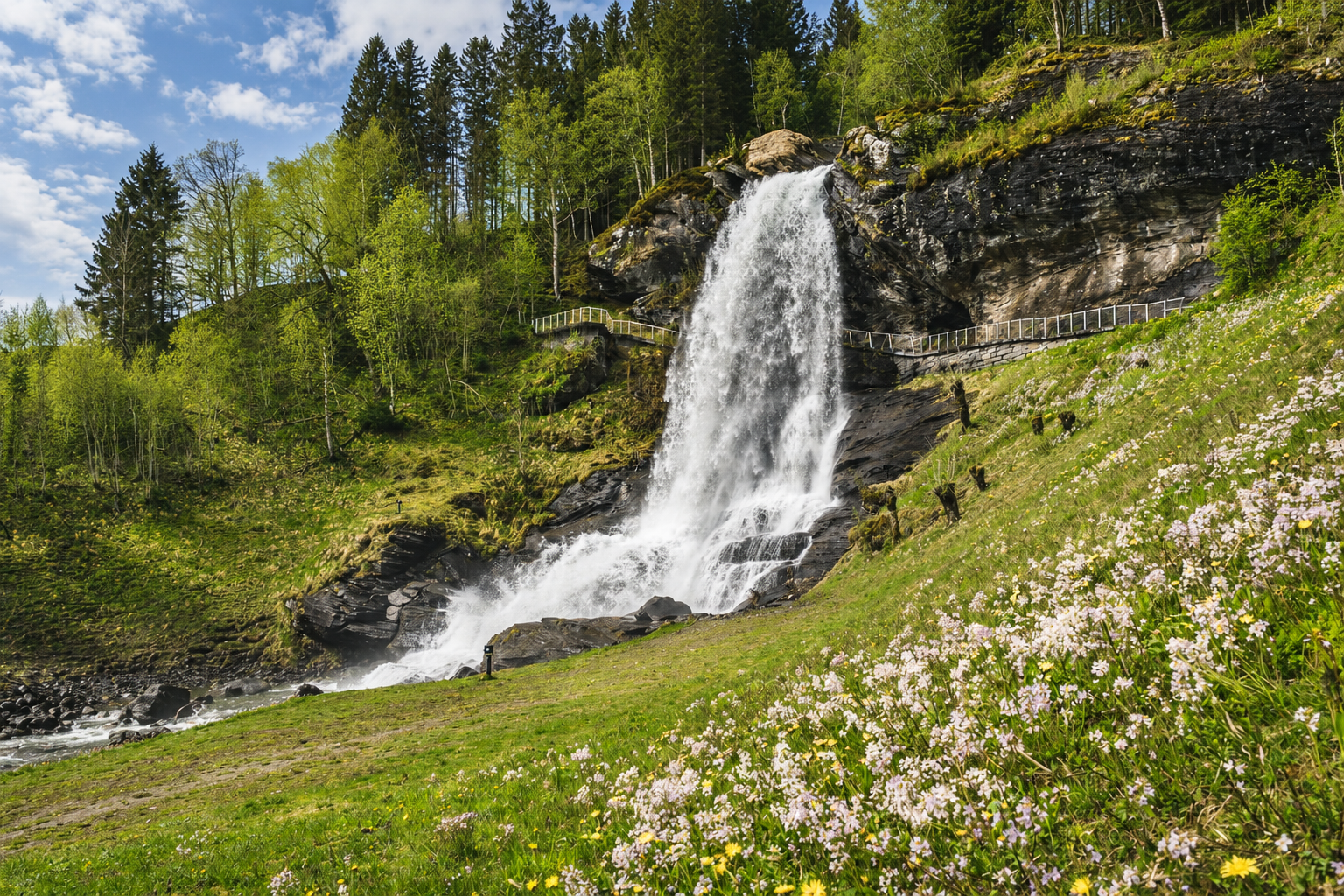 Spring waterfall flowing over a rocky slope beside fresh green vegetation in Norway